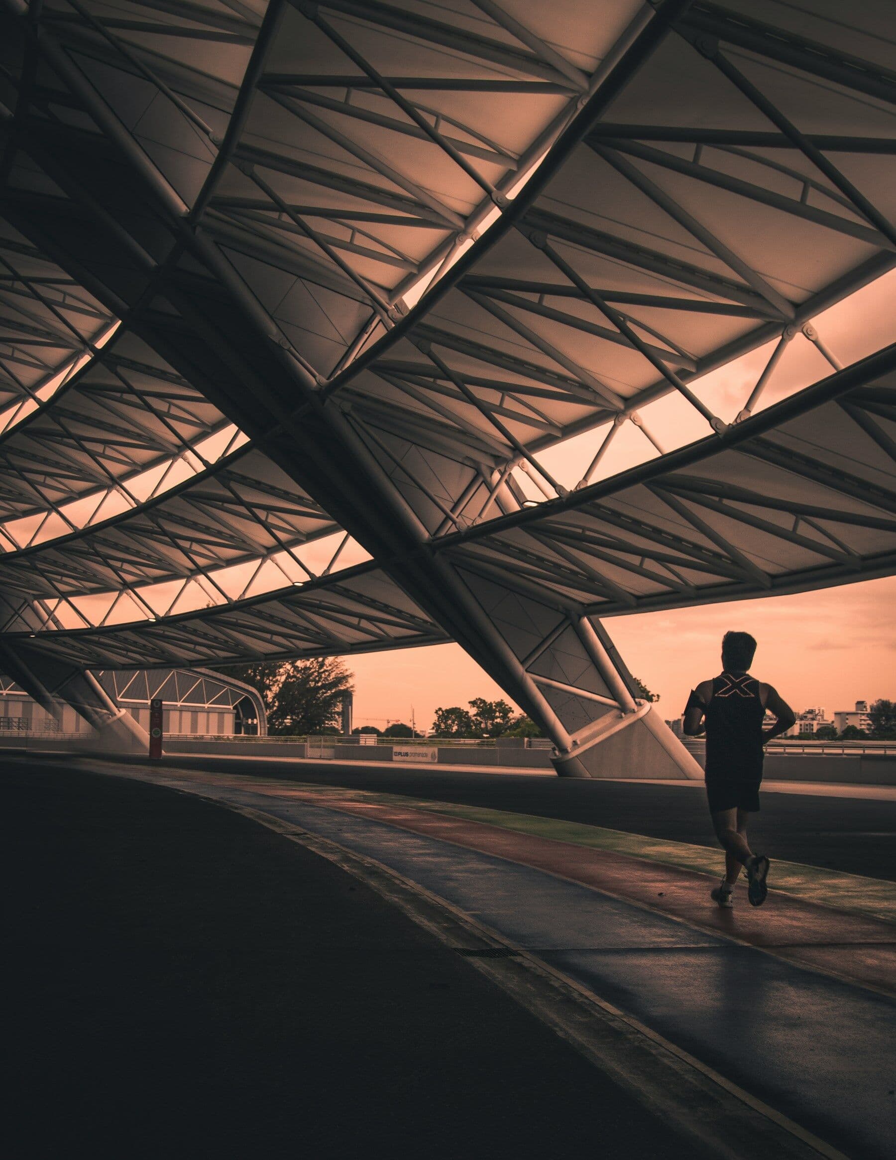 Runner on a track beneath a stadium roof at dusk
