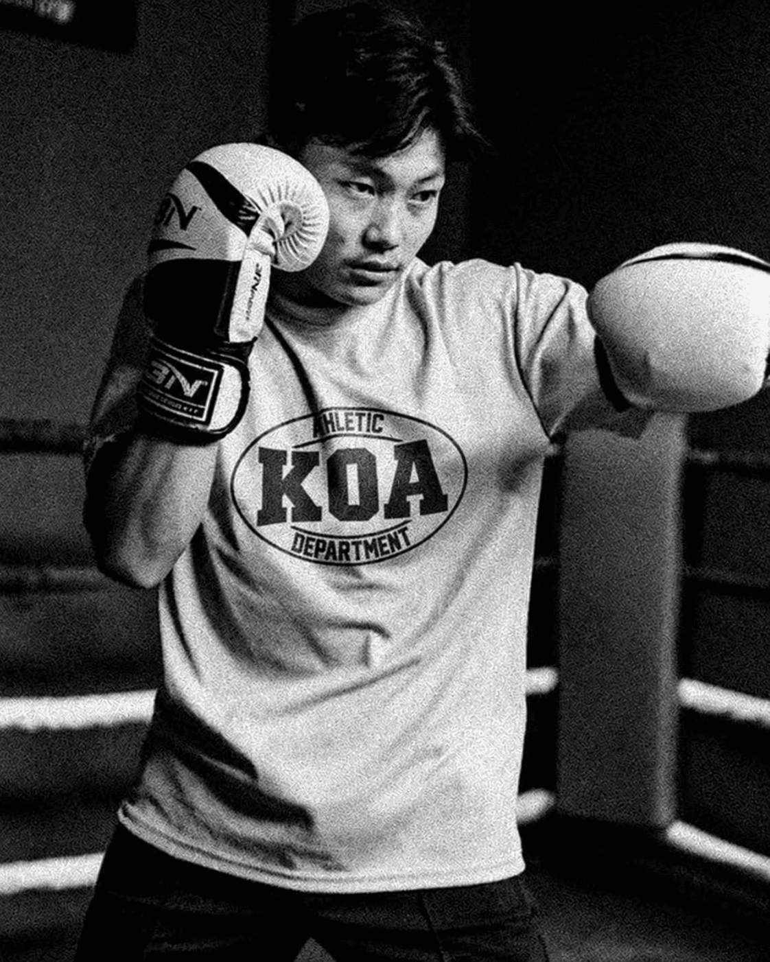 Boxer in a KOA Athletic Department tee with gloves up in a boxing ring, black-and-white